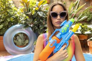 een mooi vrouw in bikini met een water pistool in een peddelen zwembad foto