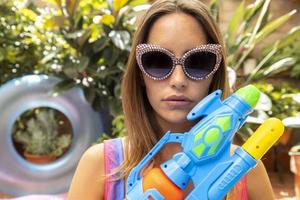 een mooi vrouw in bikini met een water pistool in een peddelen zwembad foto