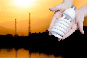 energie besparing concept, vrouw hand- Holding licht lamp Aan industrie landschap achtergrond, ideeën licht lamp in de hand- foto