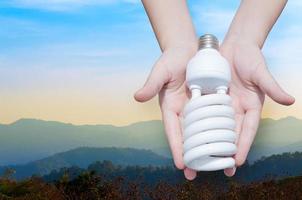 energie besparing concept, vrouw hand- Holding licht lamp Aan natuur landschap achtergrond, ideeën licht lamp in de hand- foto