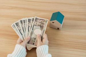 vrouw Holding Japans yen bankbiljet en huis model. echt landgoed, huis, hypotheek, Japan contant geld, belasting, recessie economie, inflatie, investering, financiën en spaargeld concepten foto