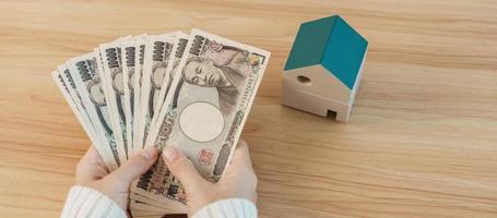 vrouw Holding Japans yen bankbiljet en huis model. echt landgoed, huis, hypotheek, Japan contant geld, belasting, recessie economie, inflatie, investering, financiën en spaargeld concepten foto