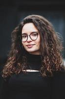 mooi jong vrouw met brunette gekruld haar, portret in oog bril genieten van de zon in de stad. foto