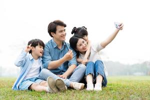 beeld van een Aziatisch familie zittend samen Aan de gras Bij de park foto