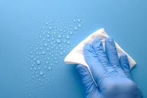 hand in blauwe rubberen handschoenen schoonmaken van waterdruppels van een blauw oppervlak foto