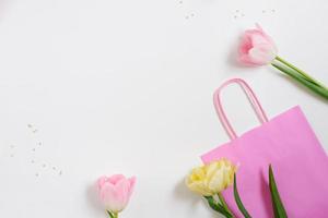 mooi voorjaar roze en geel tulpen bloemen met wit lint met helder zak Aan wit. vlak leggen. kopiëren ruimte. dames dag of valentijnsdag dag geschenk. concept van vakantie voorjaar uitverkoop in op te slaan foto