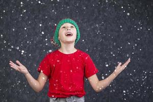 een grappig weinig jongen in een rood t-shirt vangsten de vliegend sneeuw. foto