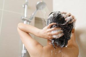 vrouw nemen douche en het wassen haar- met shampoo in badkamer Bij huis foto