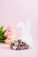 gelukkig Pasen kwartel eieren in een nest, wit konijn en tulpen Aan een roze achtergrond verticaal visie foto