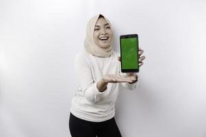 een gelukkig Aziatisch moslim vrouw vervelend een hoofddoek, tonen haar telefoon scherm, geïsoleerd door wit achtergrond foto