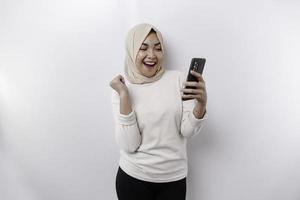 een jong Aziatisch moslim vrouw met een gelukkig geslaagd uitdrukking vervelend een hijab en Holding smartphone geïsoleerd door wit achtergrond foto