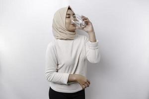 blij Aziatisch moslim vrouw vervelend hoofddoek is drinken een glas van water, geïsoleerd Aan wit achtergrond. foto