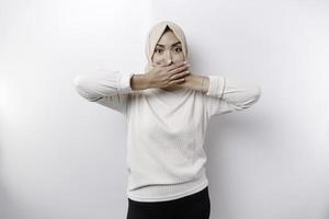 portret van een jong Aziatisch moslim vrouw vervelend een hoofddoek is vertellen worden stil, zwijgen met echt gezicht, stil met vinger ingedrukt naar lippen, geïsoleerd door wit achtergrond foto