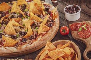 pizza met mozzarella, ui, pepperoni, zwarte olijven, groene paprika, nacho's en oregano foto