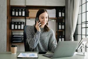 jong mooi vrouw typen Aan tablet en laptop terwijl zittend Bij de werken houten tafel kantoor foto