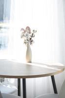 een boeket van katoen twijgen in een vaas Aan een ronde tafel met een Pasen decor van eieren en een Pasen konijn in de licht van de venster in een minimalistische interieur. foto