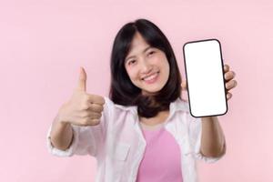 gelukkig glimlachen jong Aziatisch vrouw aanbevelen tonen nieuw toepassing of mobiel advertentie, mockup smartphone sjabloon banier geïsoleerd Aan roze achtergrond. collage blanco scherm digitaal mobiel apparaat. foto