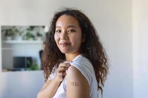 jong Aziatisch vrouw met Zelfklevend verband Aan haar arm na corona virus vaccin. eerste hulp. medisch, apotheek en gezondheidszorg concept. foto