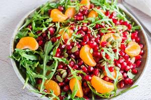 fruit vitamine salade van granaatappel, mandarijn, rucola en pompoen zaden in een bord Aan de tafel. biologisch vegetarisch voedsel. detailopname foto