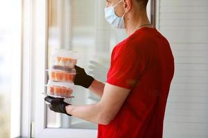 een Mens handen rubber handschoenen en medisch masker met een plastic containers met sushi en broodjes. foto