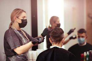 kapper met veiligheid maatregelen voor covid19, bezuinigingen een Mens in een geneeskunde masker, sociaal afstand, snijdend haar- met een medisch masker en rubber handschoenen. foto