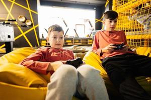 twee broers spelen video spel troosten, zittend Aan geel poef in kinderen Speel centrum. foto