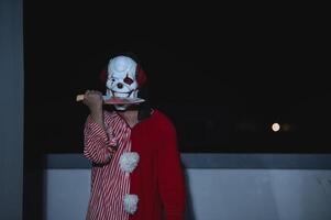 Aziatisch knap Mens slijtage clown masker met wapen Bij de nacht scène, halloween festival begrip, verschrikking eng foto van een moordenaar in oranje doek, kwaad clown karakter