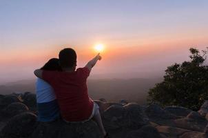 broer en zus zittend Aan rots en zien zonsondergang samen foto