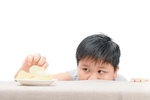 zwaarlijvig dik jongen is bereiken aardappel chips Aan tafel foto