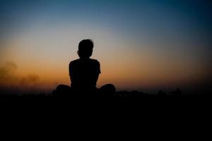 silhouet van een vrouw ga zitten met zo verdrietig in de zonsondergang. foto