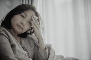 Aziatische zieke vrouw zit op de bank, blijf thuis, de vrouw voelde zich slecht, wilde gaan liggen en rusten, hoge koorts foto
