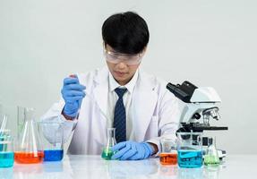 Aziatisch mannetje leerling wetenschapper in reagens menging laboratorium in een wetenschap Onderzoek laboratorium met test buizen van divers maten en microscopen. Aan de tafel in laboratorium chemie laboratorium wit achtergrond. foto