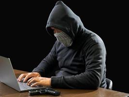 hacker spion Mens een persoon in zwart capuchon zittend Aan een tafel op zoek computer laptop gebruikt Log in wachtwoord aanval veiligheid naar circuleren gegevens digitaal in internet netwerk systeem, nacht donker achtergrond. foto