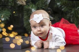 weinig baby Bij kerstmis. drie maanden oud meisje tegen de achtergrond van de Kerstmis boom decoratie. foto