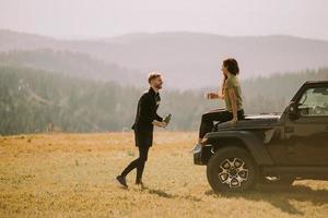 jong paar ontspannende Aan een terrein voertuig kap Bij platteland foto