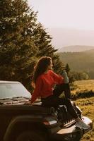 jonge vrouw ontspannen op de motorkap van een terreinvoertuig op het platteland foto