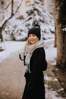 jong vrouw in warm kleren genieten van in sneeuw met meenemen koffie kop foto