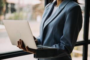 aantrekkelijk glimlachen jong Aziatisch bedrijf vrouw werk Bij huis kantoor, Aziatisch vrouw werken Aan laptop computer Holding tablet. foto