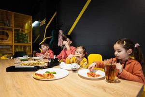 vier kinderen aan het eten Italiaans pizza in pizzeria. kinderen eten Bij cafe. foto