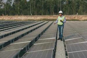 ingenieur inspecteur Holding laptop en werken in zonne- panelen macht fabriek controle fotovoltaïsche cellen en elektriciteit productie. foto