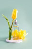 voorjaar samenstelling met een fles van delicaat parfum en geel tulp Aan een wit ronde podium. groen achtergrond. verticaal visie. foto