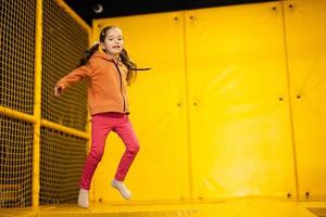 weinig meisje kind jumping Aan trampoline Bij geel speelplaats park. kind in beweging gedurende actief vermaak. foto