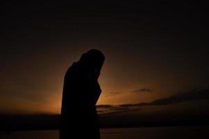 silhouet jong Aziatisch moslim Mens bidden Aan zonsondergang, ramadan festival concept foto