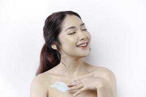 huid zorg producten concept. Aziatisch vrouw toepassen hydraterend lotion Aan lichaam na douche, staand verpakt in handdoek, bijgesneden beeld foto