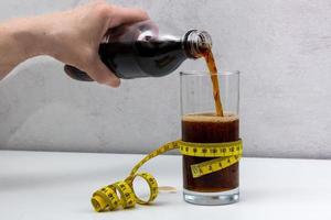 hand- giet Frisdrank in een glas verpakt in een centimeter plakband, gepast voeding, zwaarlijvigheid foto