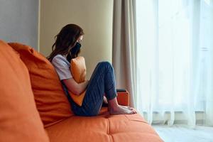 vrouw zittend Aan de oranje sofa Bij huis in beschermend maskers blijven huis concept foto