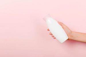vrouw hand- Holding room fles van lotion geïsoleerd. meisje geven buis kunstmatig producten Aan roze achtergrond foto