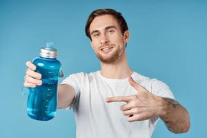 Mens in wit t-shirt water fles blussen dorst bijgesneden visie blauw achtergrond foto