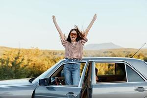 gelukkig vrouw reiziger beklommen Aan de auto en verspreiding haar armen glimlachen gelukkig. looks Bij de natuur in de omgeving van. levensstijl in reizen en vreugde foto