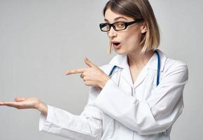 vrouw verpleegster in een medisch japon gebaren met haar handen Aan een licht achtergrond foto